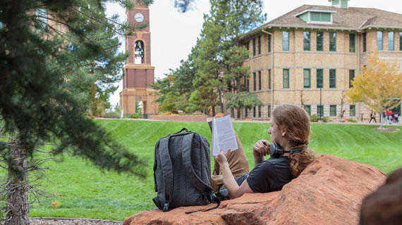 student reading book with bell tower in background