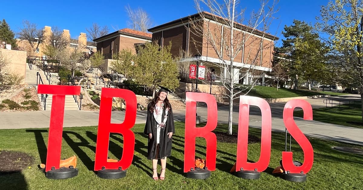 A graduate poses in between the “T-Bird” Letters on campus