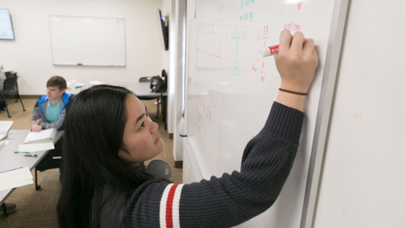 engineering student Kelly Pelicano writing equations on the whiteboard