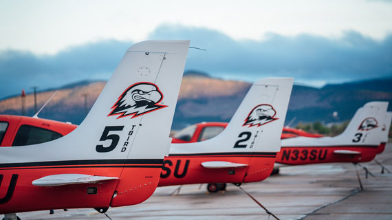 SUU planes lined up on the runway. Planes are red and white with the SUU birdhead logo on the tail